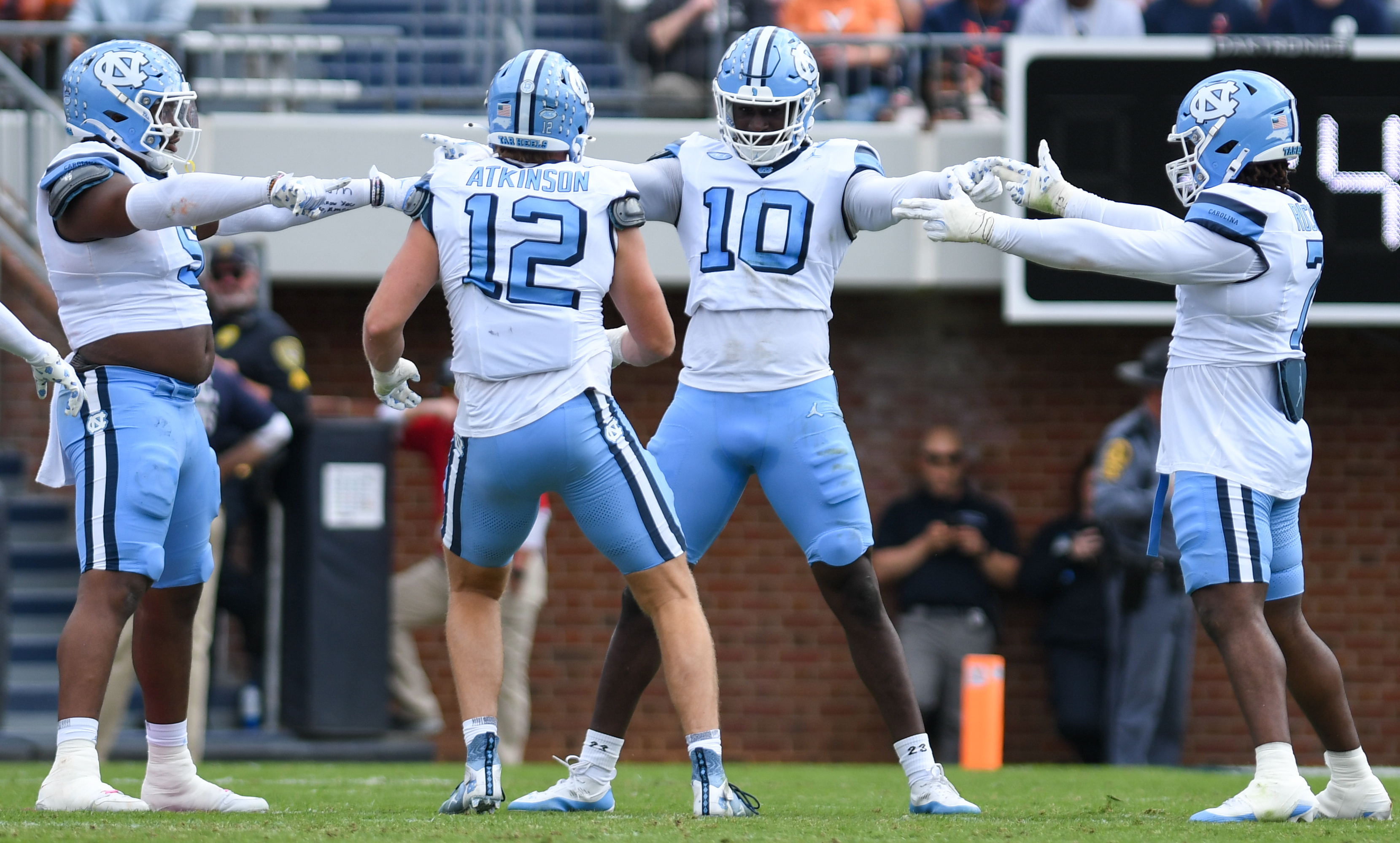 UNC Football players Atkinson, Rucker, Evans, and Ritzie pointing at each other in a circle on the football field after a play.